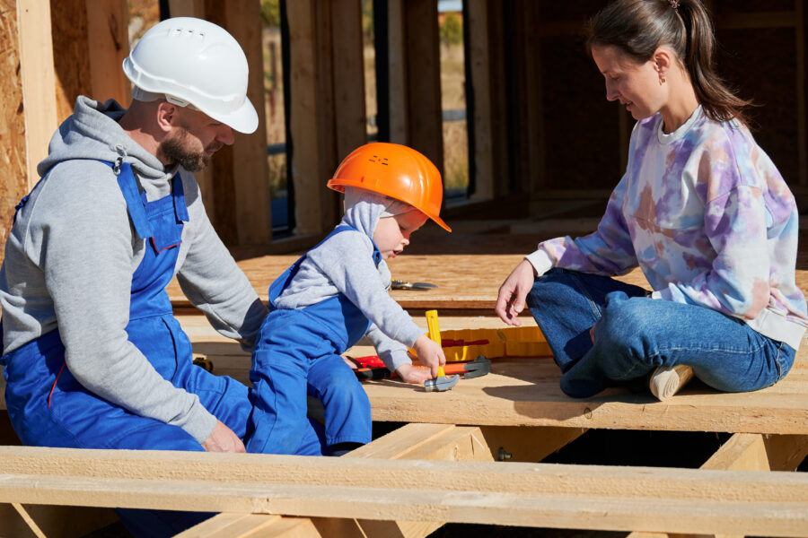 Father, mother and son building wooden frame house.