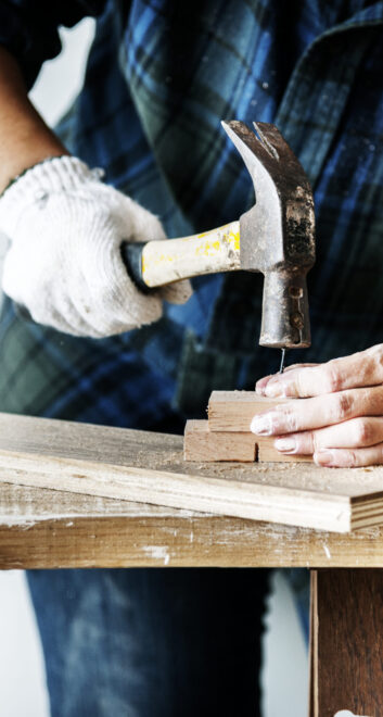 Woman carpenter using hammer pushing nail on a wood